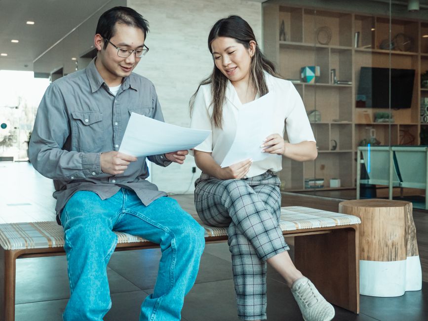 Two colleagues sitting and discussing documents in a contemporary office setting.